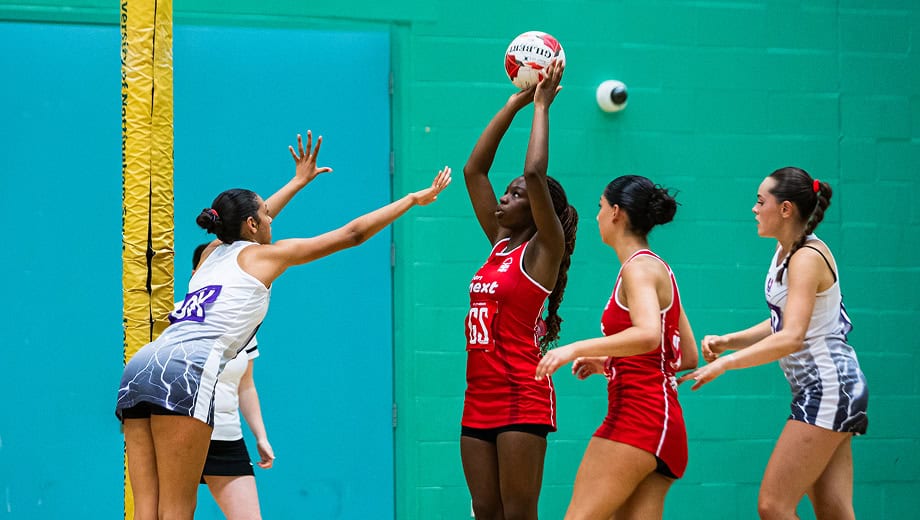 Netball player concentrates while holding the ball above her head in preperation to shoot. Opposition player is in front of here attempting to distract her.