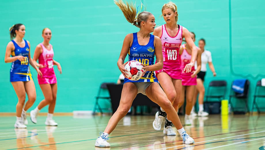 Netball player holding the ball while looking around for a team mate to pass too.