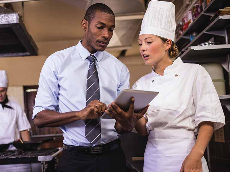 Manager looking at an iPad while taking to a chef in a kitchen