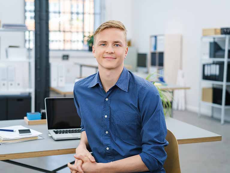 A male looking at camera sitting at an office desk
