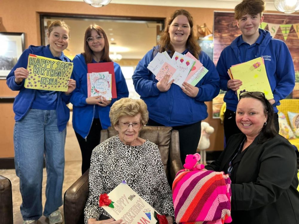 Four Loughborough College students stand behind staff member Susan and Edna, celebrating her 100th birthday