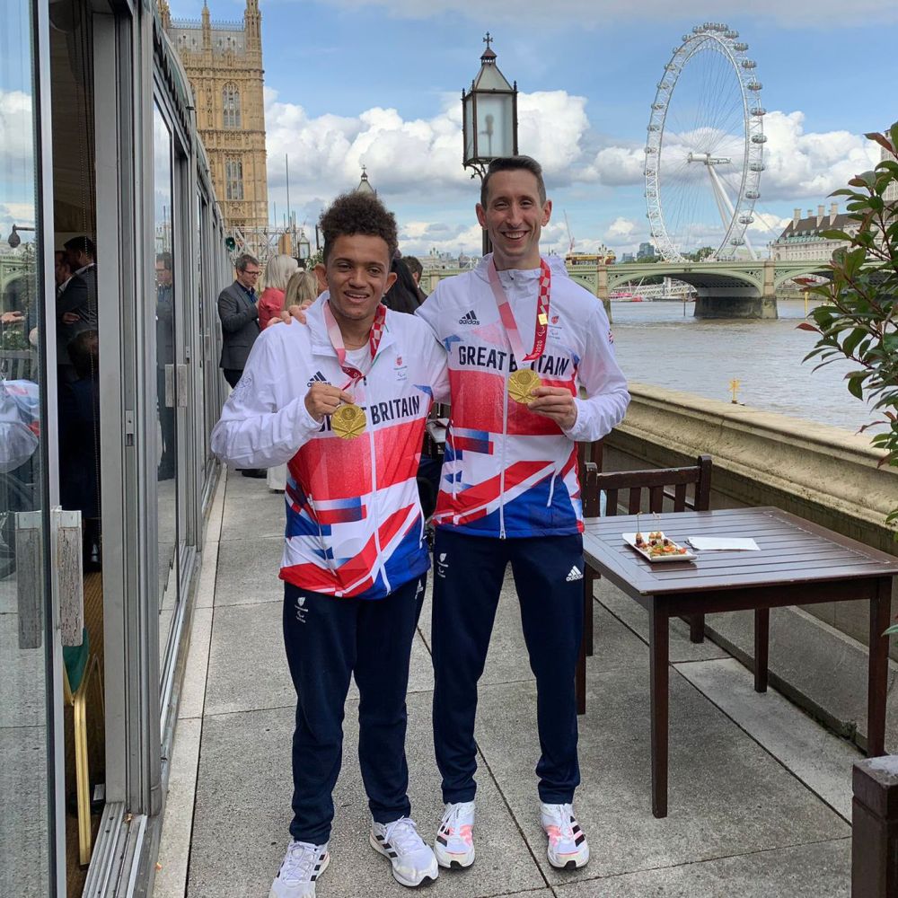 Tom Young and Jonathan Broom-Edwards holding dressed in their Paralympic uniforms holding their gold medals outside a London scenescape