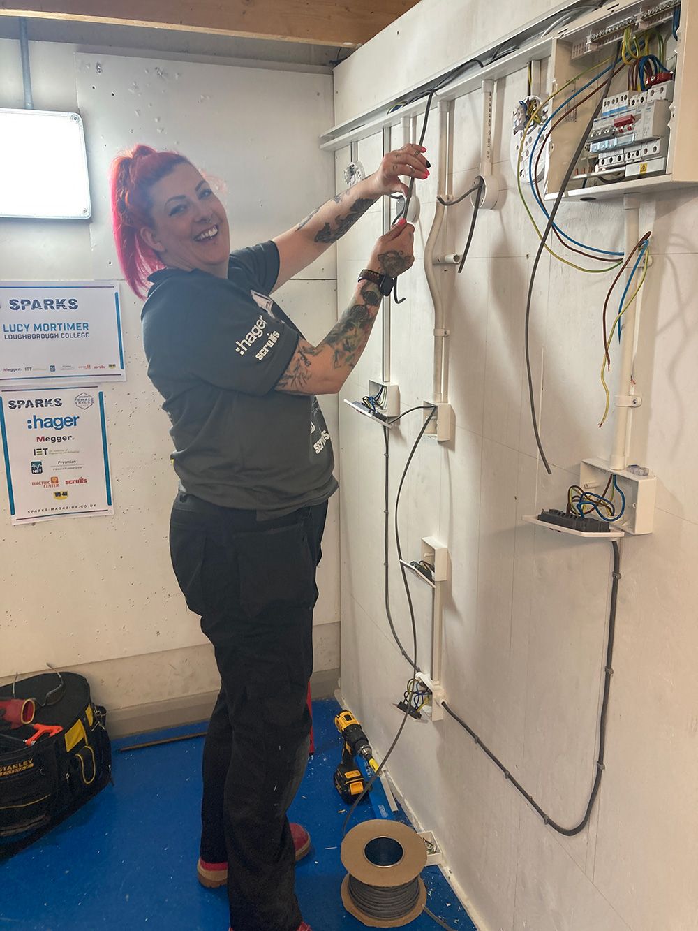 A Student taking place in the SPARKS final, moving an electrical cable through trunking attached to the wall towards a junction box